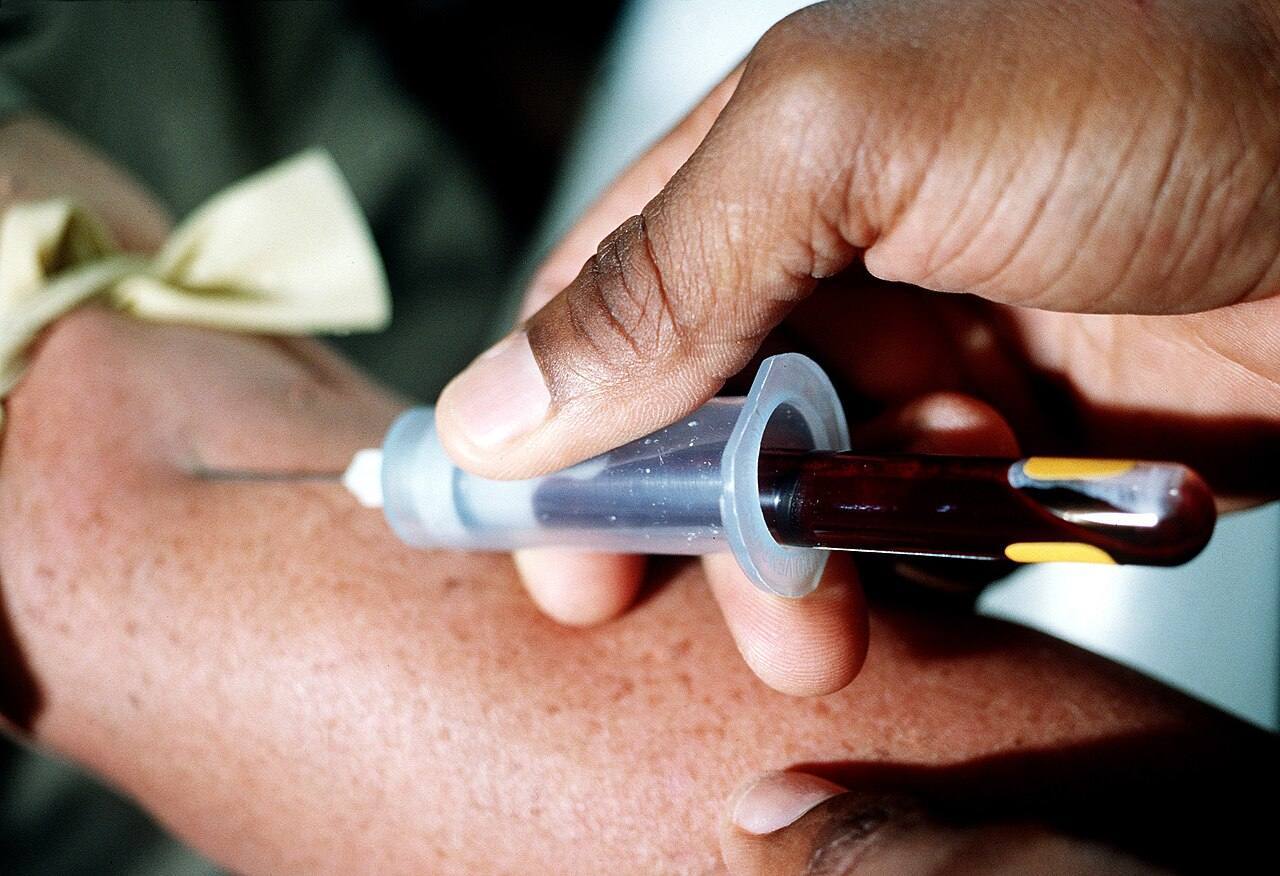 A corpsman uses a syringe to draw a patient's blood for testing at the naval hospital