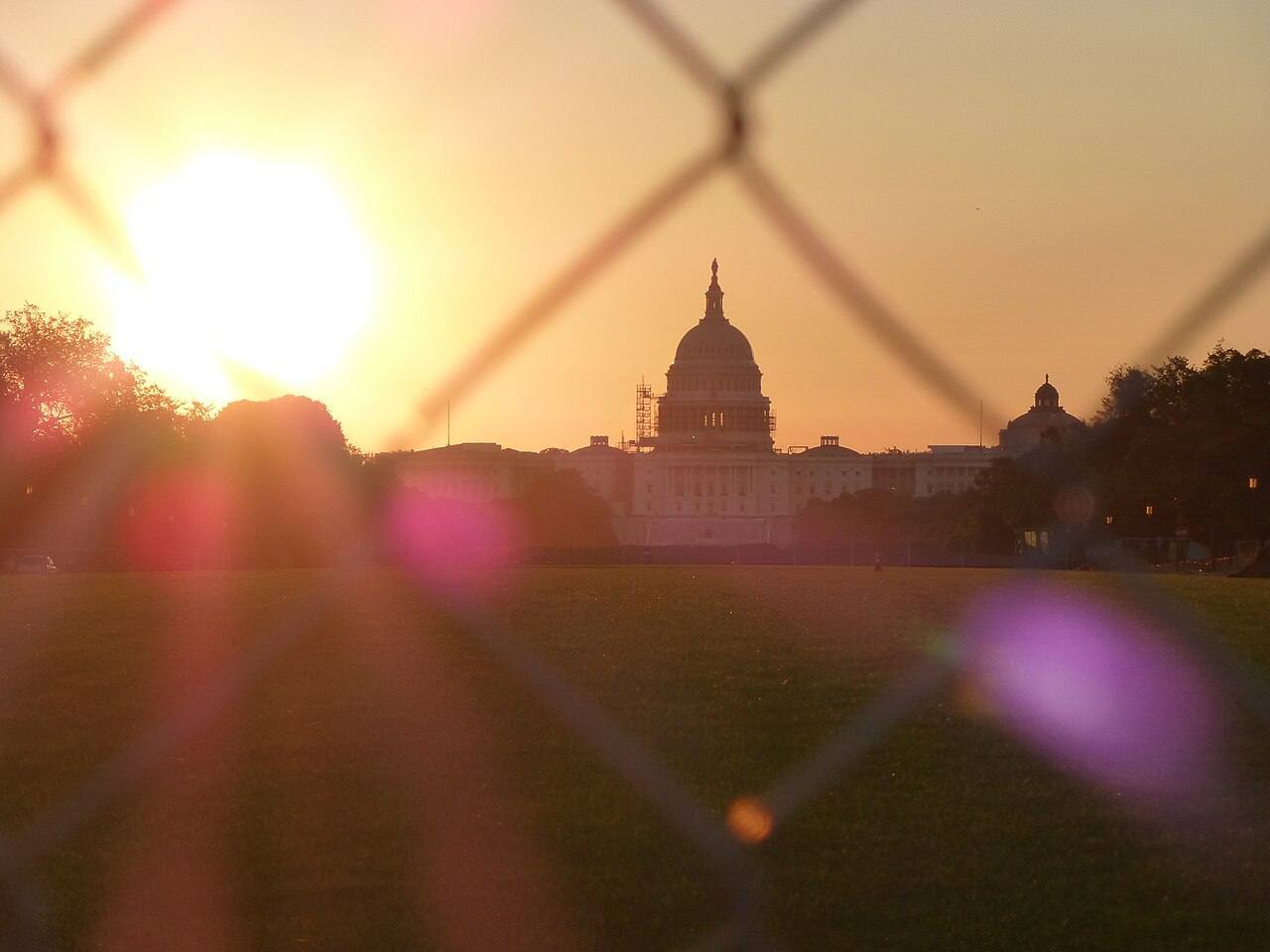 United States Capitol shot through fence at sunrise.